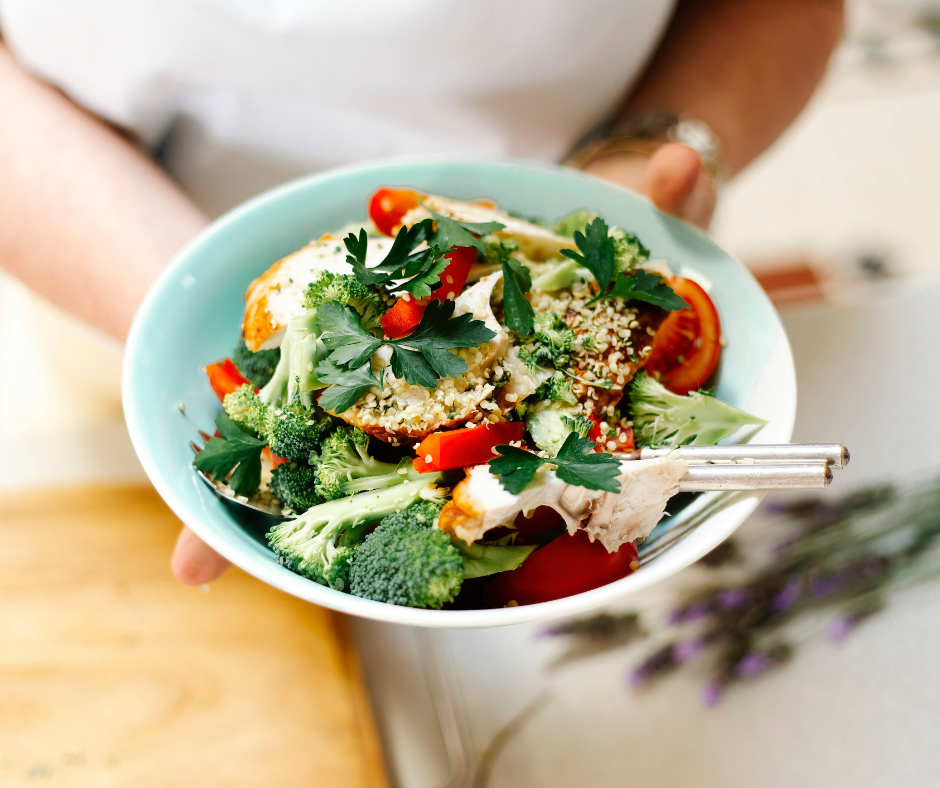 A fresh bowl of chicken, broccoli, capsicum and herbs being held in two hands