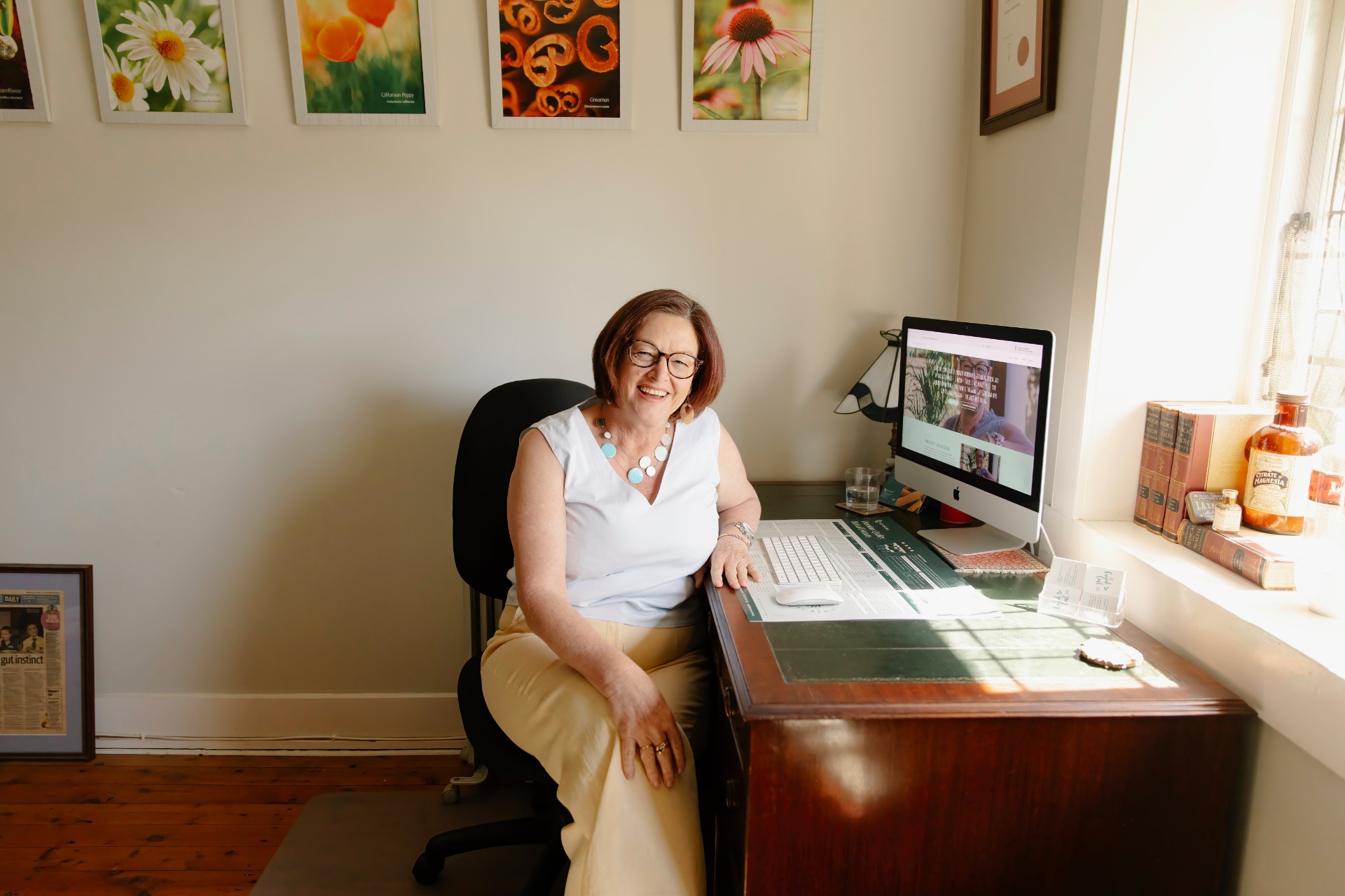 Sharon Hespe at her naturopathic office desk surrounded by botanical prints and apothecary jars