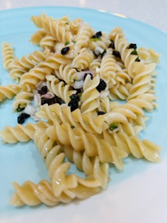 Spiral pasta salad with olives and fresh herbs on a turquoise plate